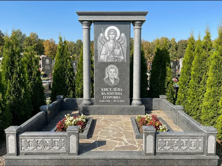 Памятник с гравировкой иконы: массивная стела с двускатным навершием-домиком — гравировка Николая Чудотворца, живая изгородь из туи, работа «Журавлёв» в Екатеринбурге