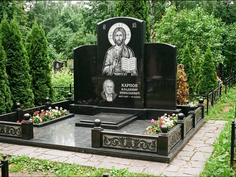 Памятник с гравировкой иконы: широкая панорамная стела с золочёным нимбом — гравировка образа Матроны Московской, цветник с белыми хризантемами, работа «Мельникова» в Екатеринбурге