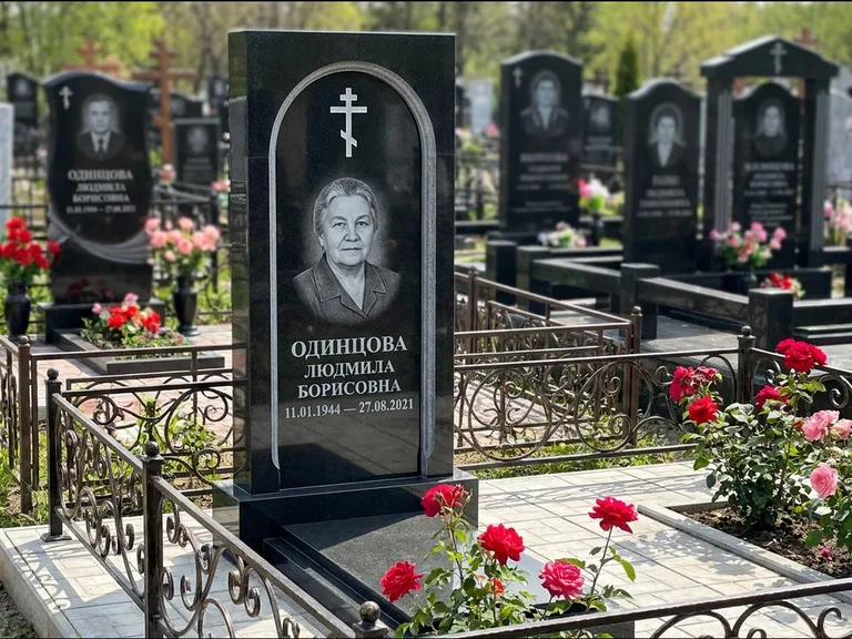 Памятник из чёрного гранита — скромная невысокая стела с крестом с терновым венцом, работа «Лаврентьева» в Екатеринбурге